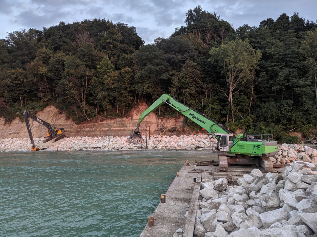 two front loaders installing rock revetment along the shore